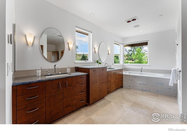 bathroom featuring tile patterned floors, two vanities, a bath, and a sink