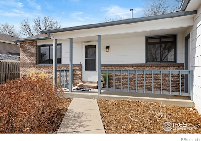 doorway to property featuring a porch, fence, and brick siding