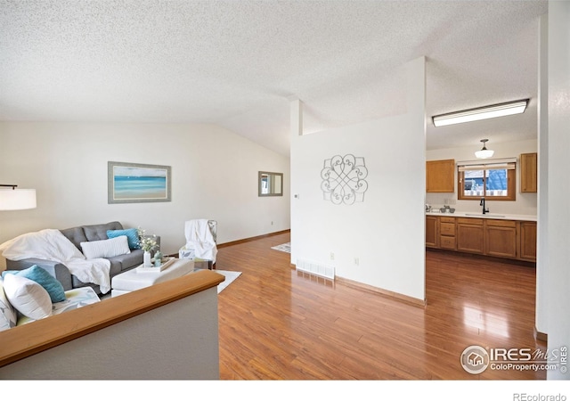 living room featuring lofted ceiling, wood finished floors, visible vents, and a textured ceiling