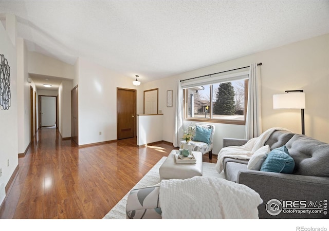 living area with a textured ceiling, baseboards, lofted ceiling, and wood finished floors