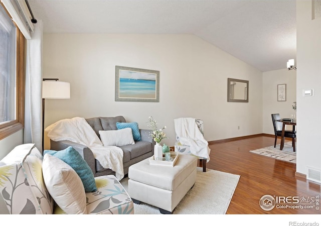 living room with lofted ceiling, wood finished floors, visible vents, and baseboards