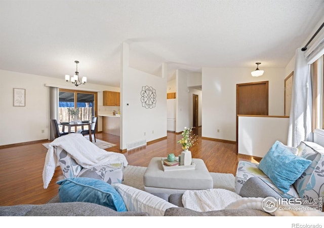 living area with baseboards, lofted ceiling, an inviting chandelier, and wood finished floors