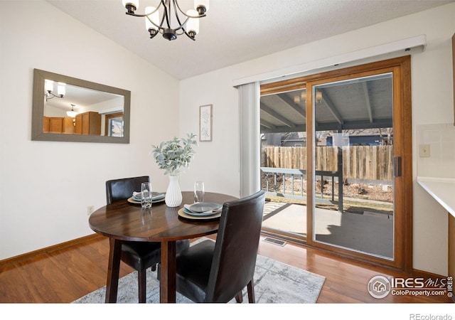 dining area with a chandelier, visible vents, wood finished floors, and vaulted ceiling