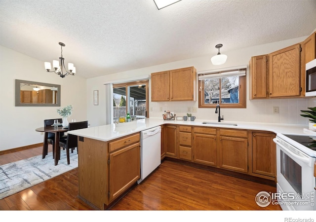 kitchen featuring a notable chandelier, a sink, white appliances, a peninsula, and dark wood-style flooring