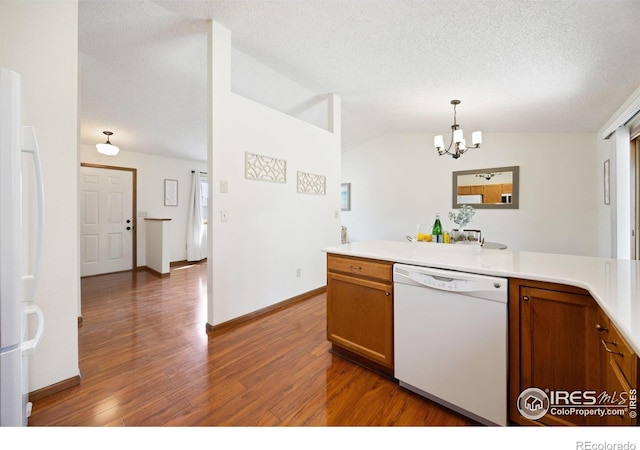 kitchen featuring white appliances, wood finished floors, brown cabinetry, an inviting chandelier, and vaulted ceiling