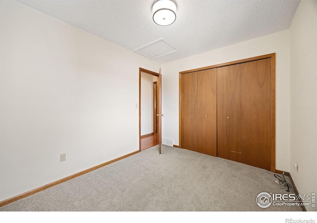 unfurnished bedroom with carpet, baseboards, attic access, a closet, and a textured ceiling