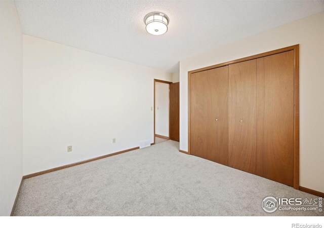 unfurnished bedroom featuring a closet, carpet floors, a textured ceiling, and baseboards