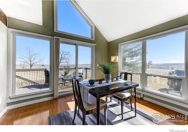 dining area with high vaulted ceiling, baseboards, and wood finished floors