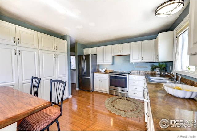 kitchen with light wood-type flooring, appliances with stainless steel finishes, white cabinets, wood counters, and a sink