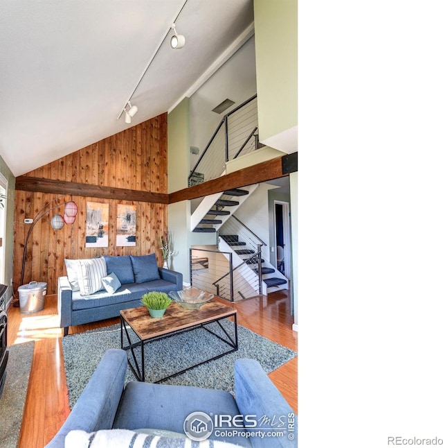 living room featuring stairway, wood finished floors, high vaulted ceiling, track lighting, and wood walls