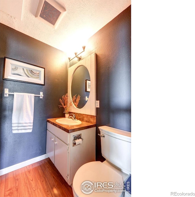 bathroom with visible vents, toilet, wood finished floors, and a textured wall