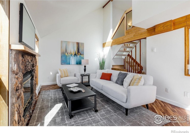 living room with wood finished floors, baseboards, high vaulted ceiling, stairs, and a glass covered fireplace