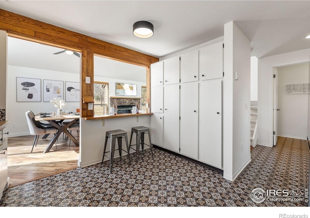 kitchen featuring baseboards, a breakfast bar, a fireplace, white cabinets, and tasteful backsplash