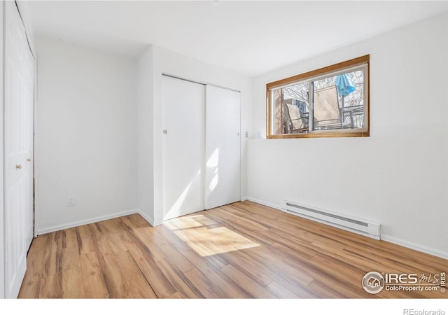 unfurnished bedroom with a closet, wood finished floors, baseboards, and a baseboard radiator