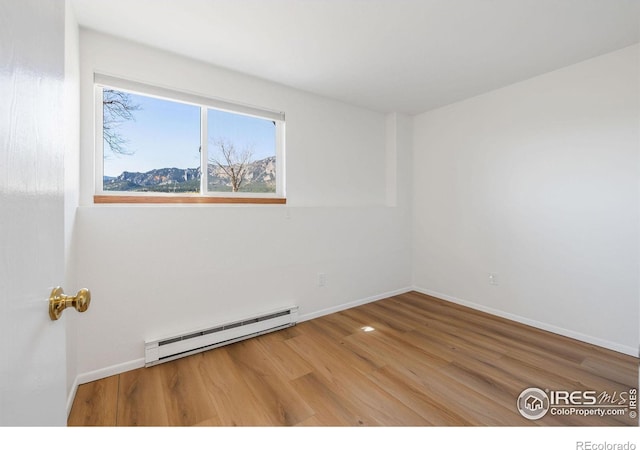 unfurnished room with a baseboard heating unit, baseboards, and wood finished floors