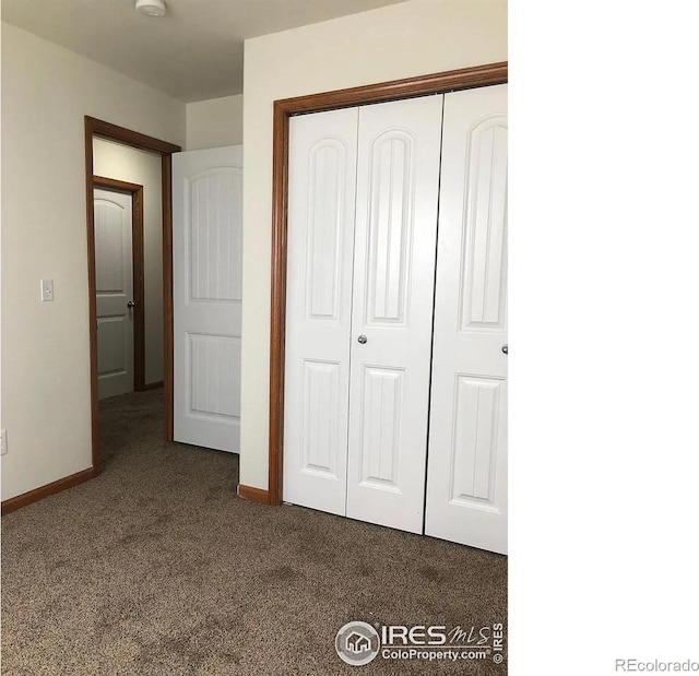 unfurnished bedroom with a closet, baseboards, and dark colored carpet