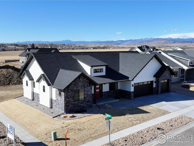 modern farmhouse with roof with shingles, a mountain view, a garage, stone siding, and board and batten siding