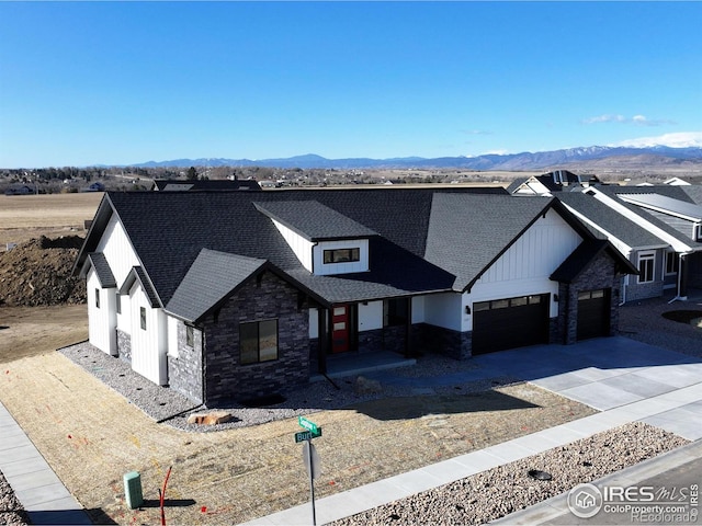 modern inspired farmhouse featuring a garage, stone siding, roof with shingles, and a mountain view