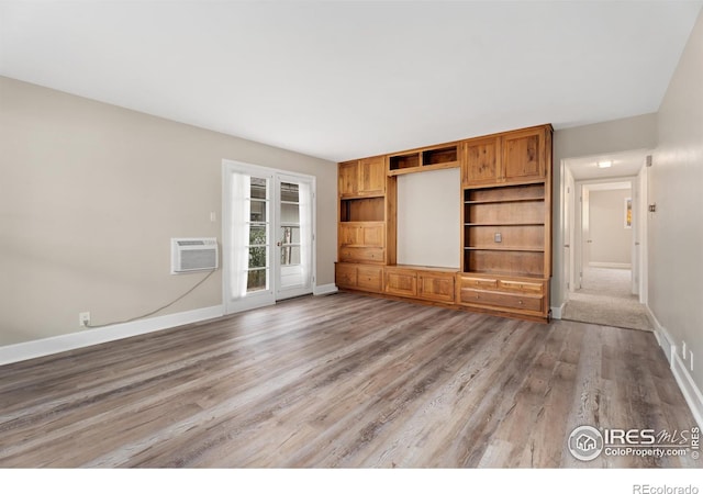 unfurnished living room featuring a wall unit AC, light wood-style floors, and baseboards