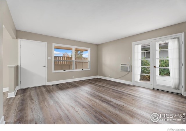 interior space with an AC wall unit, wood finished floors, baseboards, and a wealth of natural light