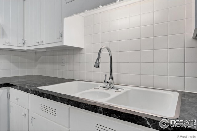 kitchen featuring dark countertops, white cabinets, tasteful backsplash, and a sink