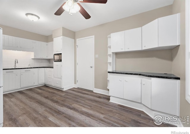 kitchen featuring dark countertops, backsplash, black microwave, dark wood finished floors, and white cabinetry