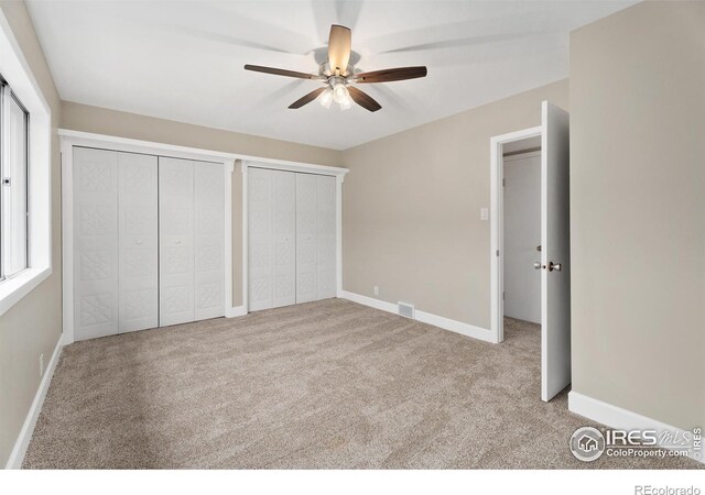 unfurnished bedroom featuring carpet flooring, visible vents, baseboards, and multiple closets