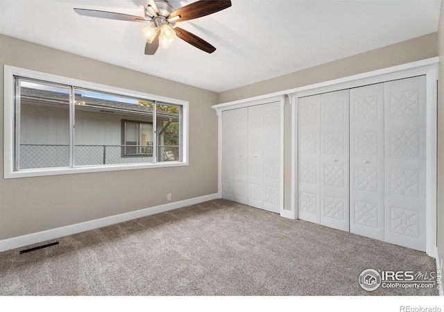 unfurnished bedroom featuring a ceiling fan, visible vents, baseboards, carpet floors, and multiple closets