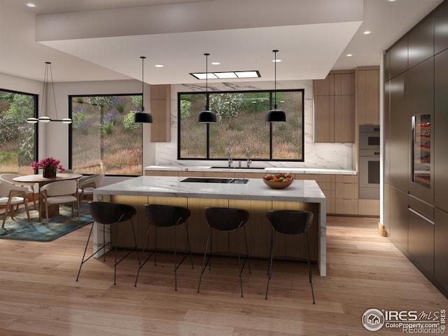 kitchen featuring light wood-type flooring, a large island, modern cabinets, backsplash, and a breakfast bar area