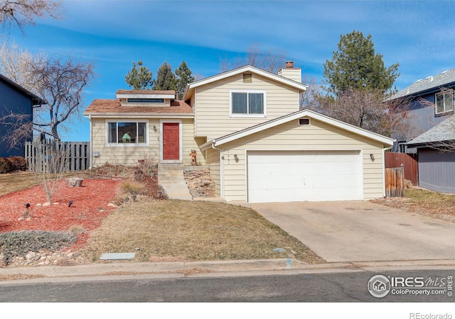 split level home featuring a garage, a chimney, driveway, and fence