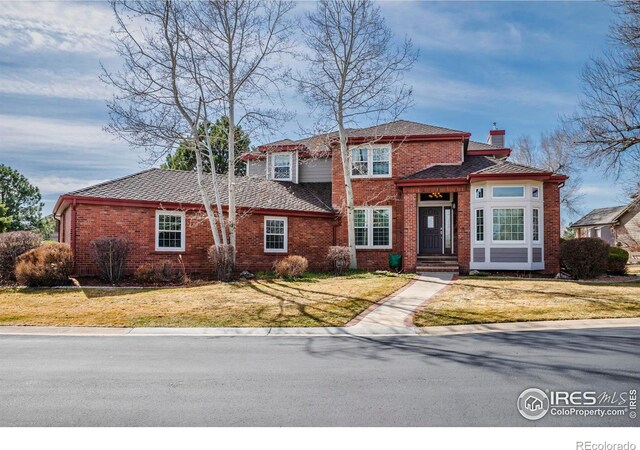 view of front of property featuring a front yard, brick siding, and a chimney