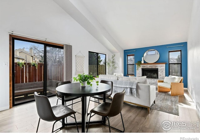 dining room featuring a brick fireplace, light wood-style flooring, baseboards, and high vaulted ceiling