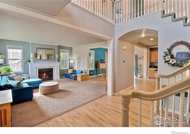 living area with arched walkways, a warm lit fireplace, stairs, and light wood finished floors