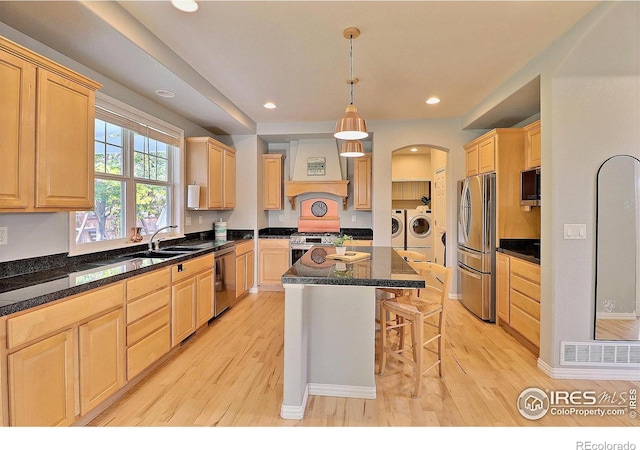 kitchen with custom range hood, independent washer and dryer, light brown cabinetry, and stainless steel appliances