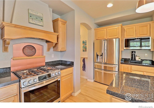 kitchen with premium range hood, light brown cabinets, stainless steel appliances, arched walkways, and light wood finished floors