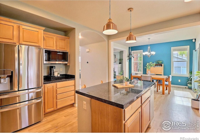 kitchen featuring dark countertops, a center island, stainless steel appliances, arched walkways, and light wood-style floors