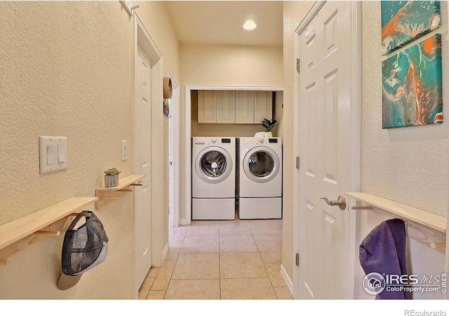 laundry area featuring washer and dryer, light tile patterned floors, cabinet space, and a textured wall