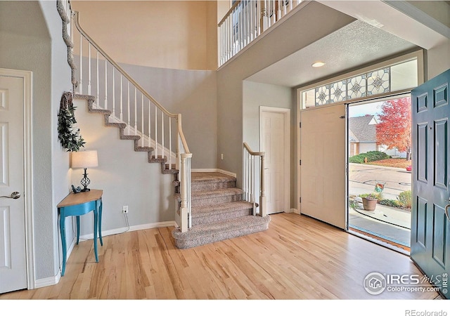 entryway featuring baseboards, a high ceiling, wood finished floors, and stairs