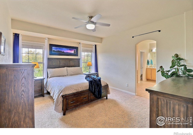 bedroom featuring ensuite bath, arched walkways, baseboards, light colored carpet, and ceiling fan