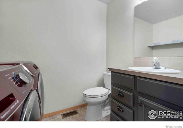 bathroom featuring visible vents, backsplash, washing machine and dryer, toilet, and vanity