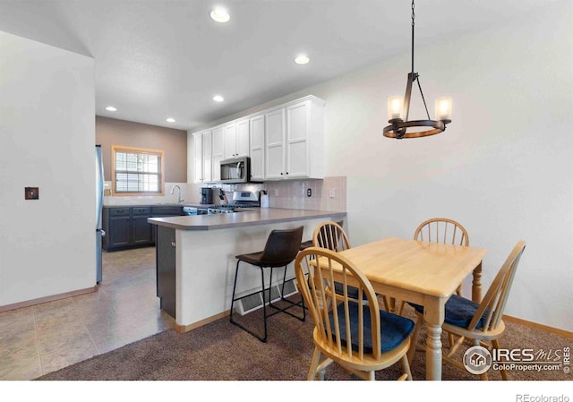 kitchen featuring a sink, appliances with stainless steel finishes, a peninsula, white cabinets, and decorative backsplash