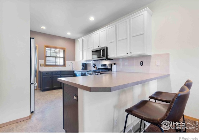 kitchen with stainless steel appliances, backsplash, a peninsula, and white cabinets