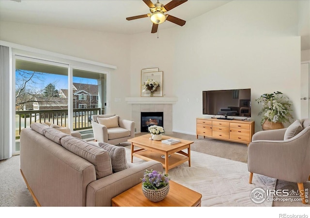 living area with a tiled fireplace, high vaulted ceiling, ceiling fan, and light carpet