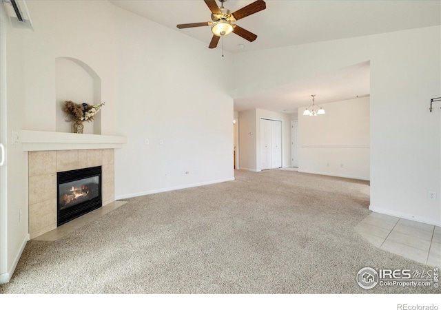 unfurnished living room featuring baseboards, a tile fireplace, vaulted ceiling, carpet flooring, and ceiling fan with notable chandelier