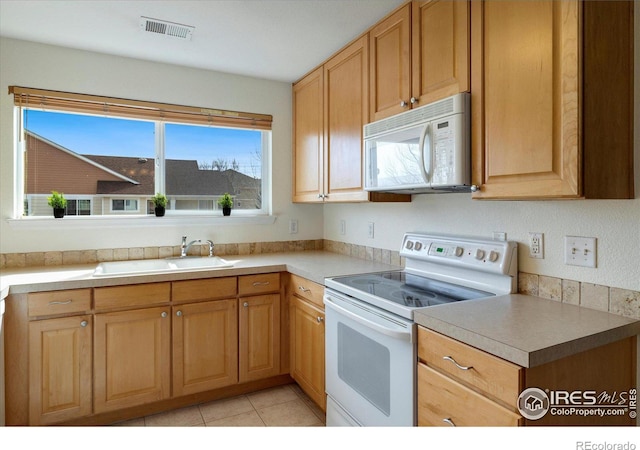 kitchen featuring visible vents, light brown cabinets, light countertops, white appliances, and a sink