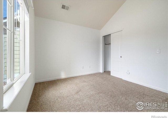 unfurnished bedroom with visible vents, multiple windows, carpet flooring, and lofted ceiling