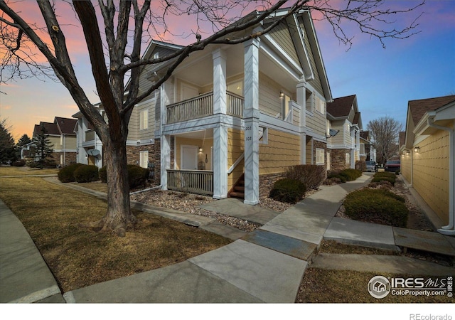 property exterior at dusk featuring stone siding and a balcony