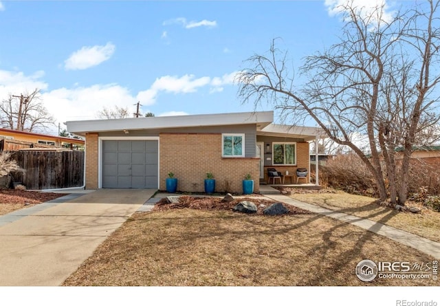 view of front of house with brick siding, concrete driveway, an attached garage, and fence