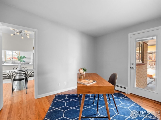 home office with light wood finished floors, a baseboard heating unit, baseboards, and a sink