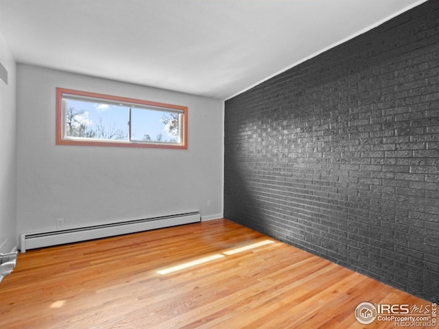 unfurnished room featuring a baseboard heating unit, wood finished floors, and brick wall